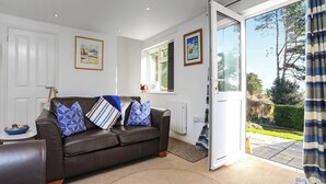 A living room with a brown leather sofa, blue patterned cushions, a white radiator, and a view of a garden through a glass door.