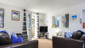 A living room with two leather sofas, a television, and a radio. There are curtains, a window, and a door leading outside.