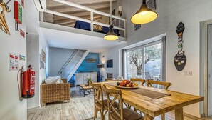 Un comedor con una mesa y sillas de madera, un banco de mimbre y vistas al exterior a través de un amplio ventanal.