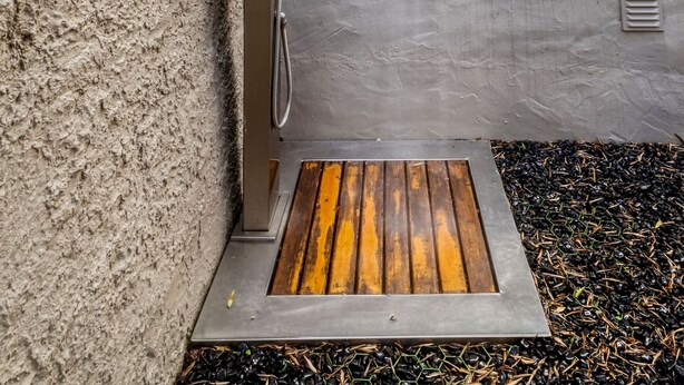 Una ducha al aire libre moderna con estructura metálica, un escalón de madera y suelo de hormigón.
