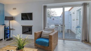 Una sala de estar acogedora con un sofá de mimbre, una chimenea, un televisor y un amplio ventanal corredera que da a un patio exterior.