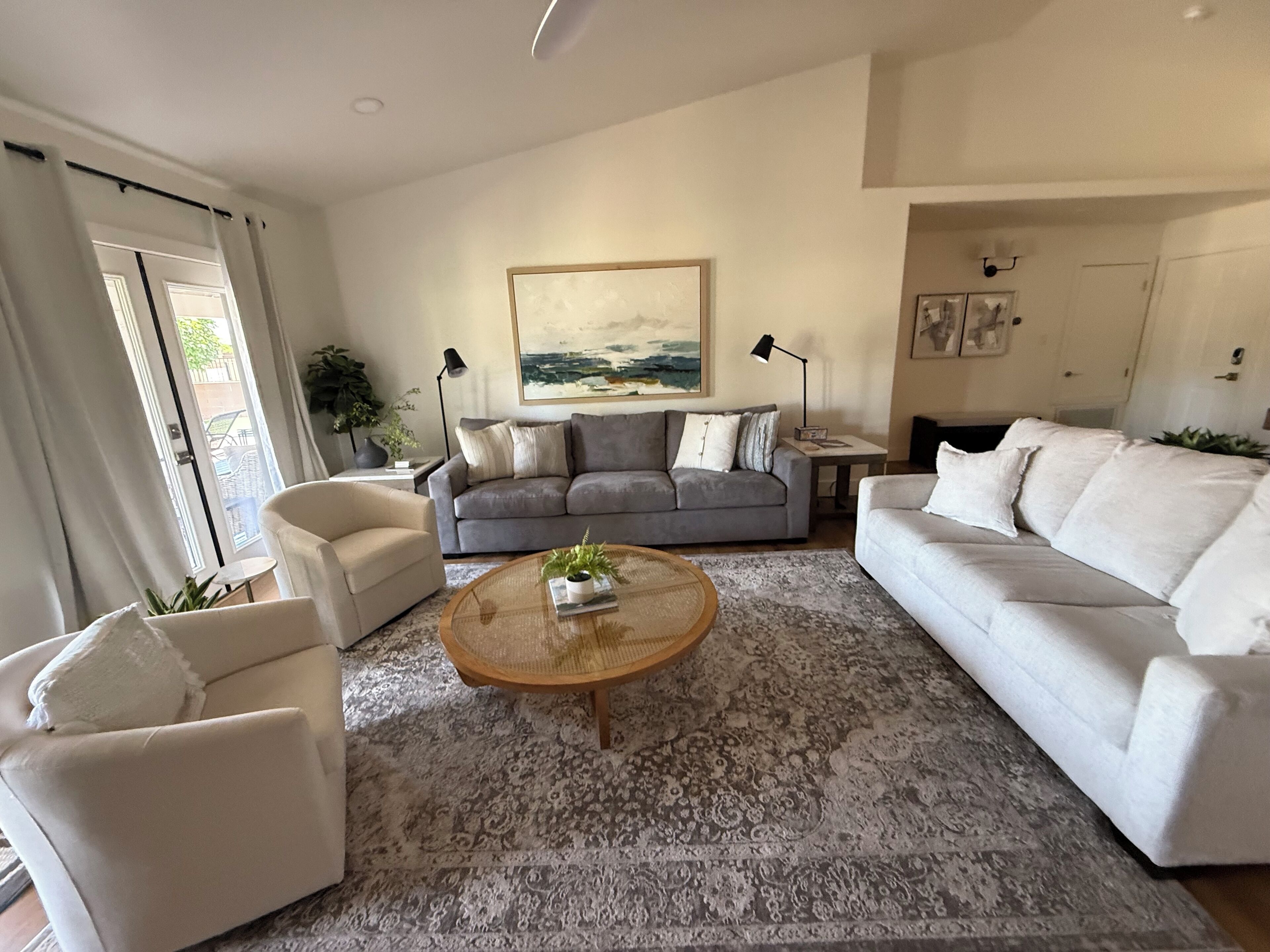 A modern living room with a grey sofa, white armchairs, a round coffee table, and a large painting on the wall.
