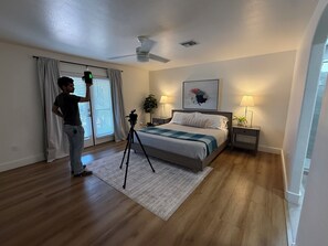 A bedroom with a bed, a standing lamp, a ceiling fan, and a window with curtains.