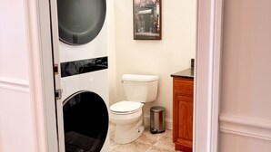 A compact bathroom with a washing machine, toilet, and trash can. - Luxurious 2 BR Loft  (Utica)