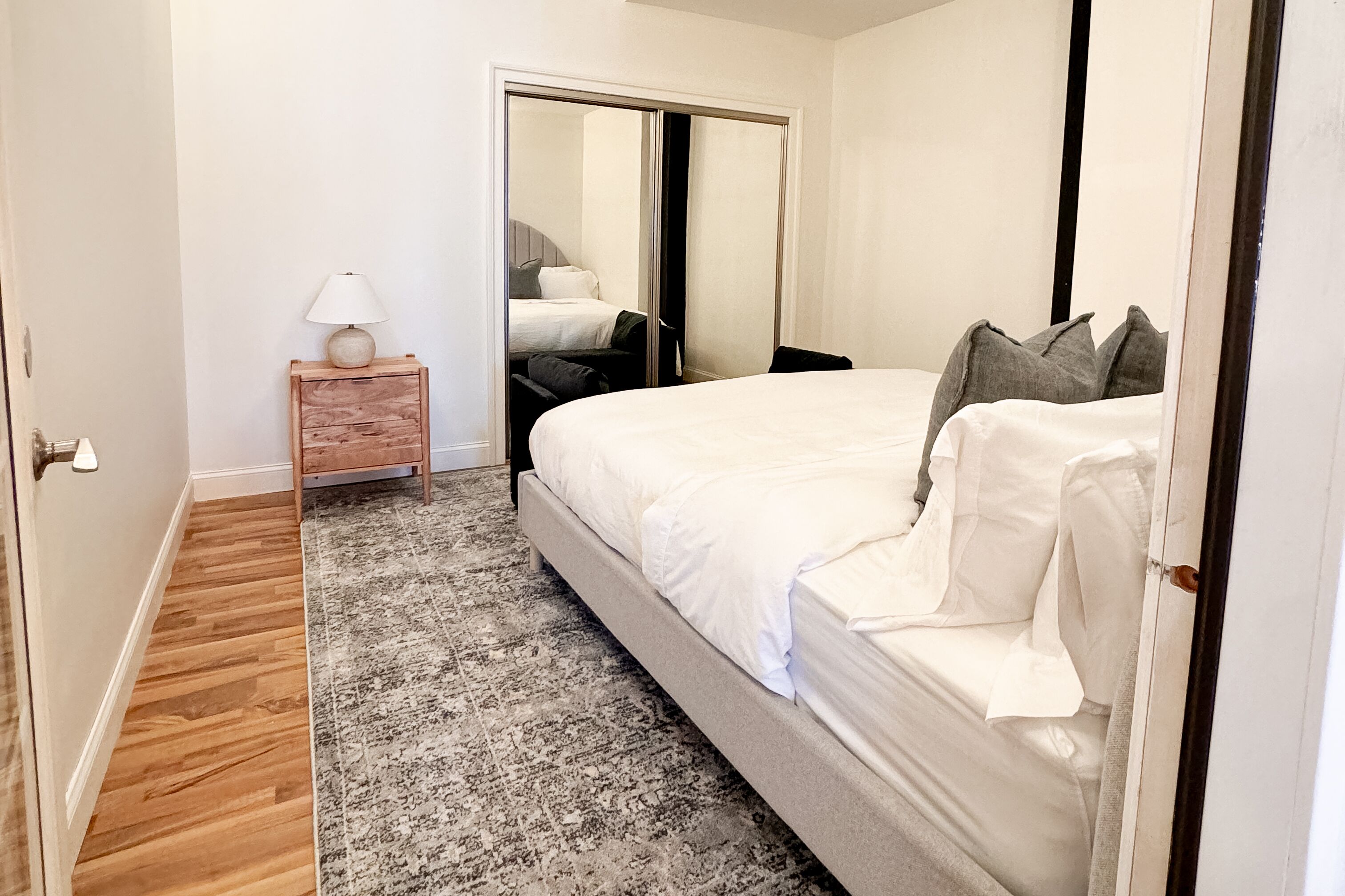 Una camera da letto con un grande letto, un comodino con una lampada, un pavimento in legno e un tappeto decorato.