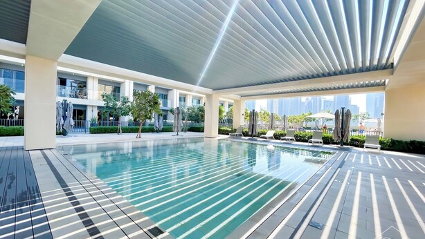 A modern indoor pool area with clear water, tiled flooring, and a ceiling with linear light fixtures.