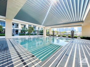 Ein moderner, überdachter Poolbereich mit klarem Wasser, Fliesenböden und einer Decke mit linear angeordneten Leuchten.