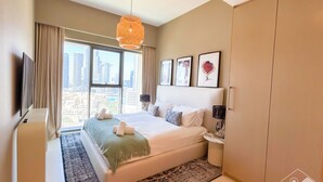A modern bedroom with a large bed, a view of the city through the window, and a mounted TV.