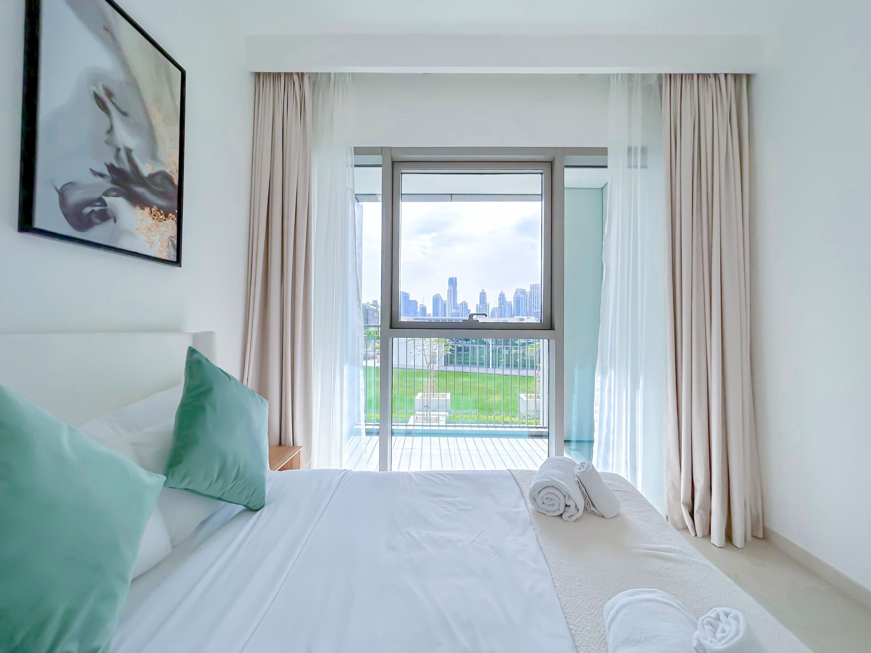 Een hotelkamer met een bed, uitzicht op een stadsbeeld door een groot raam, en een balkon met een leuning.