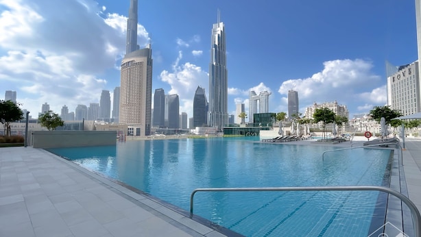 Una piscina con agua azul cristalina, rodeada por una terraza con baldosas. Al fondo, se observan edificios altos, incluyendo el Burj Khalifa.