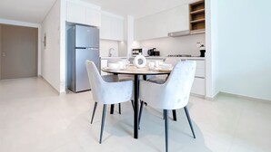 Una cocina moderna con armarios blancos, un refrigerador de acero inoxidable y una zona de comedor con una mesa redonda y dos sillas.