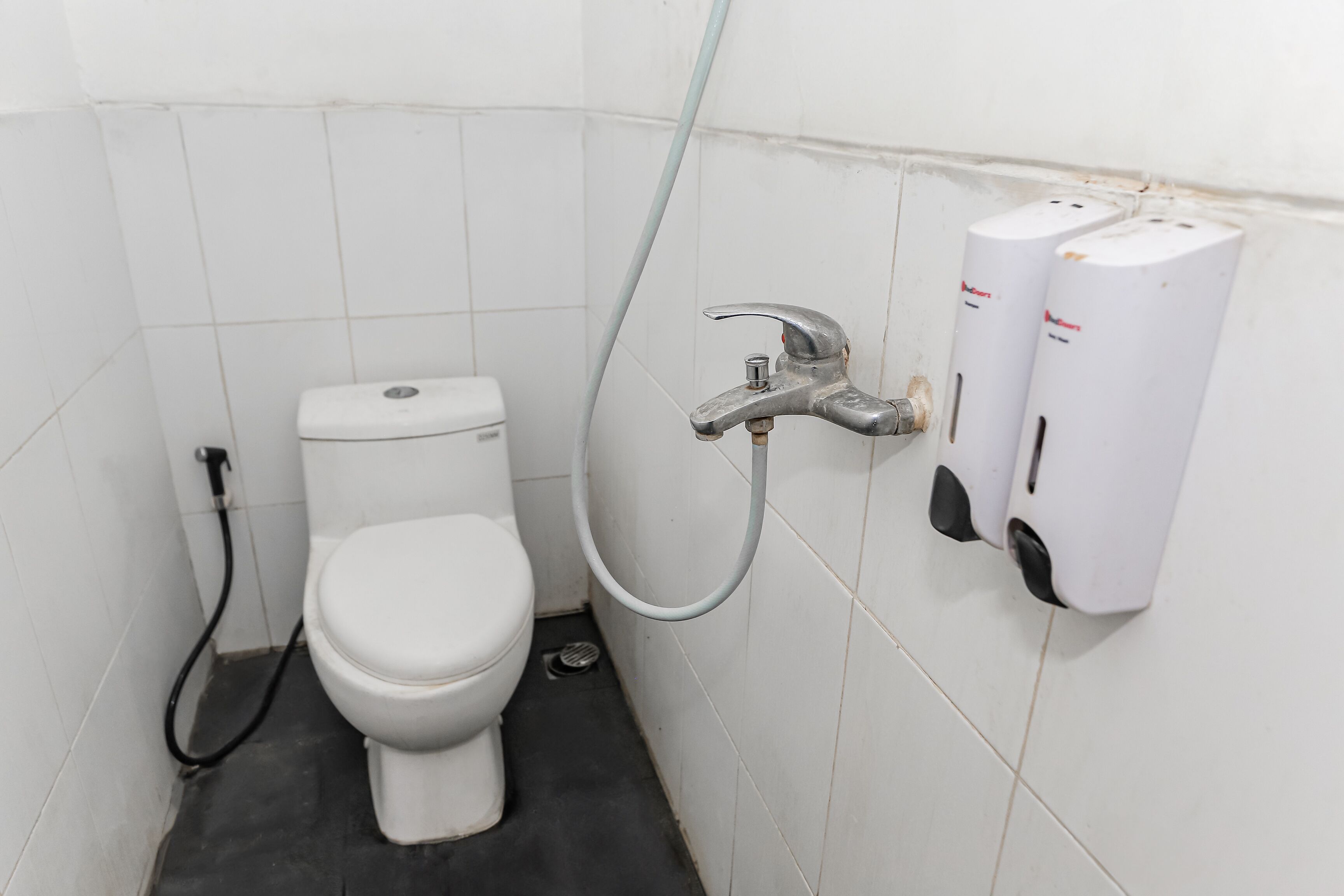A small, clean bathroom with a toilet, a handheld showerhead, and a soap dispenser.