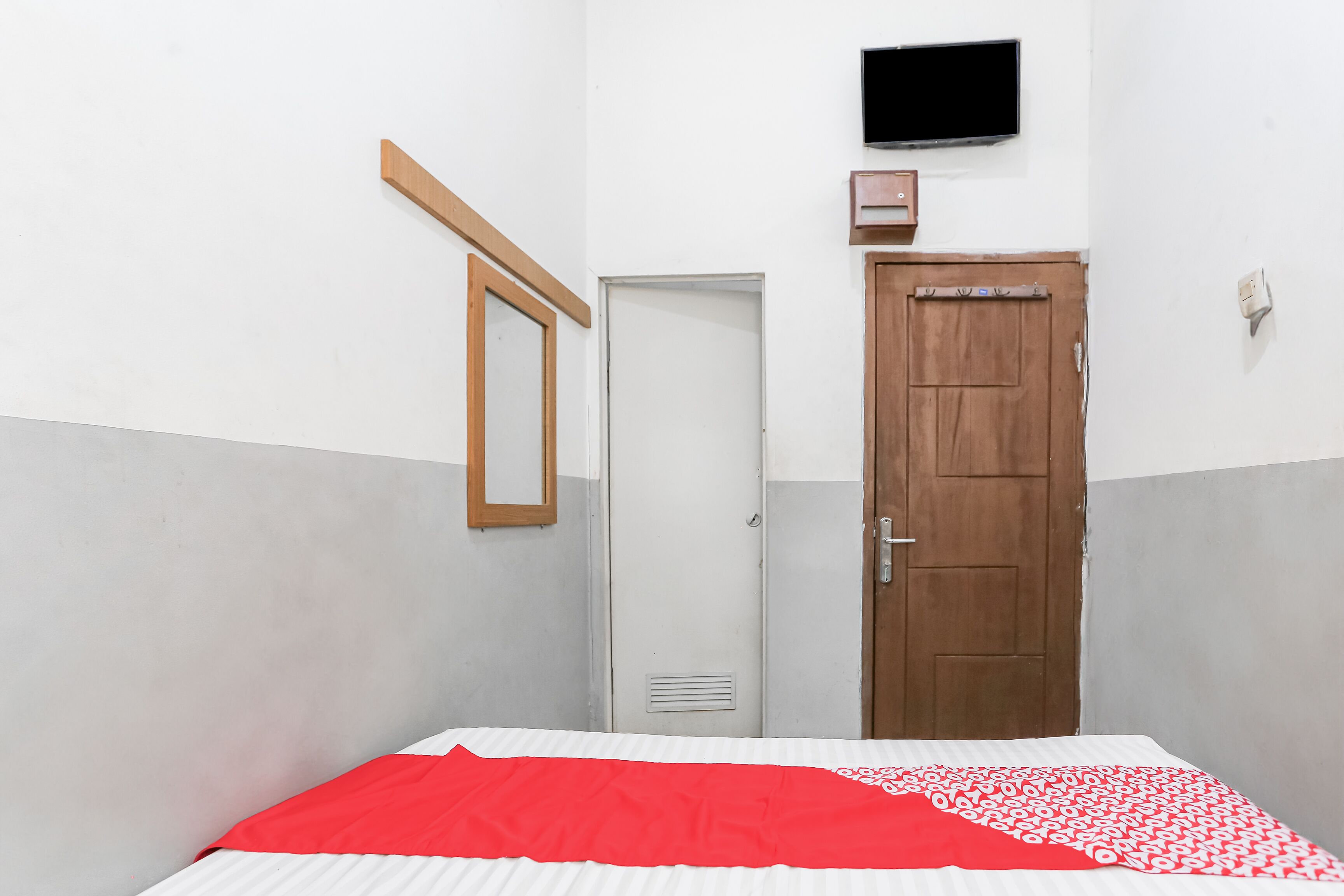 Une pièce comprenant un lit, une porte en bois, une armoire blanche et un téléviseur fixé au mur.