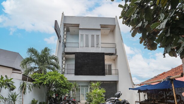 A multi-story building with a flat facade, a covered entrance, and several potted plants around the entrance.
