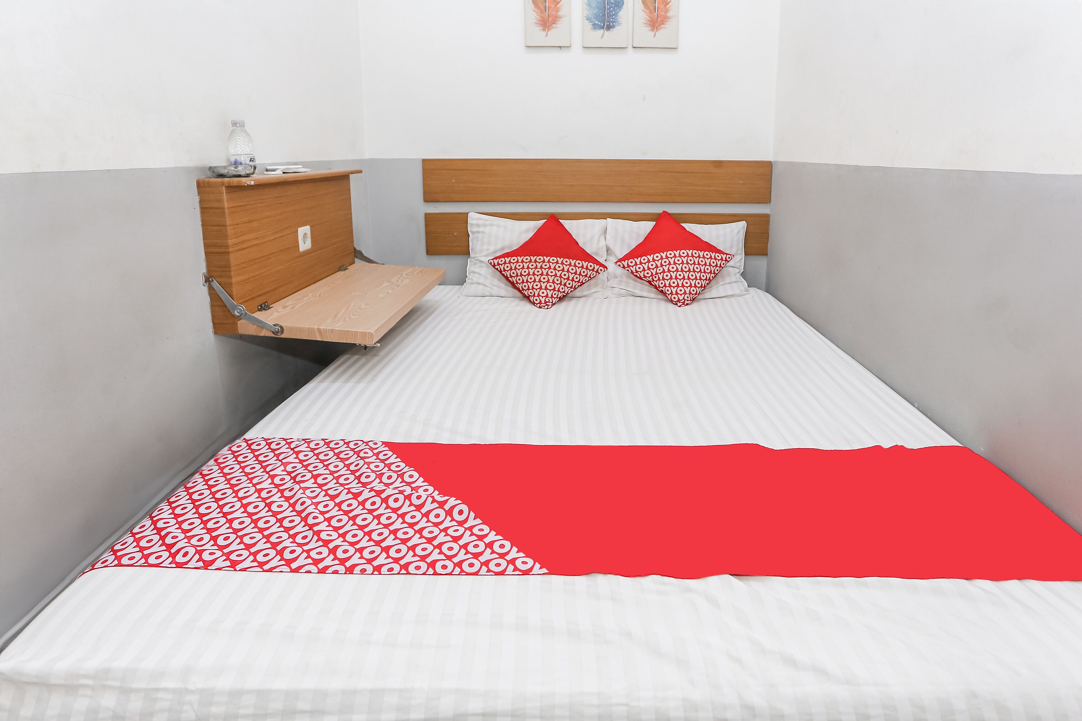 Un lit avec une couvre-lit à motifs rouges et blancs, deux oreillers rouges et une tête de lit en bois.