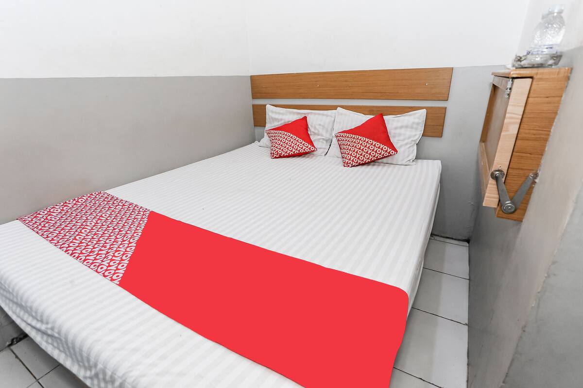 A bed with a white and red bedspread, two red and white pillows, and a wooden headboard.