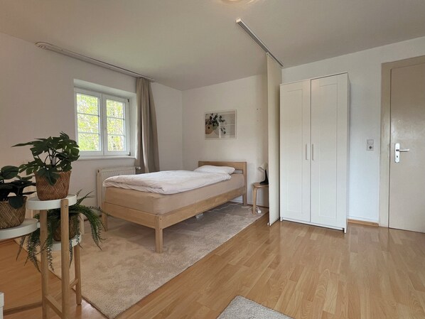 Une chambre à coucher avec un lit, une fenêtre, un radiateur, une armoire et une plante en pot.