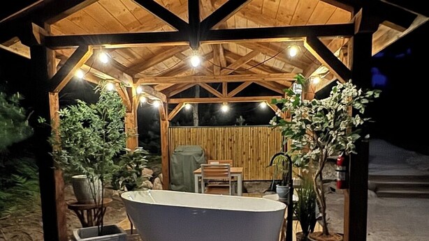 A wooden gazebo with a bathtub, seating, and potted plants. - Traverse City - Luxury on the Edge - 10 (Williamsburg)