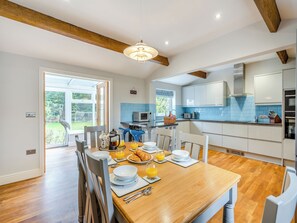 A modern kitchen with white cabinets, blue backsplash, and wooden beams. There is a dining table set with plates, glasses, and croissants.