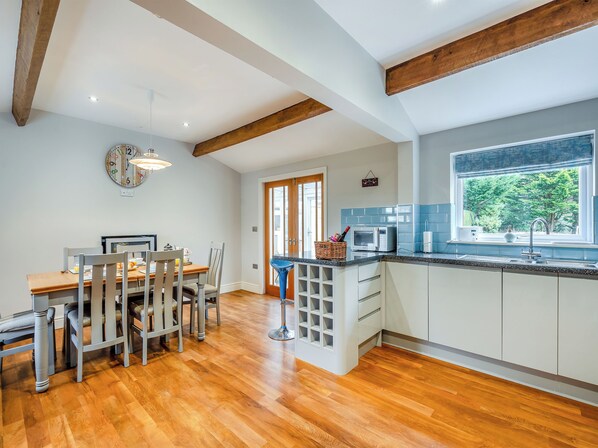 A modern kitchen with wooden beams, a dining area with a wooden table and chairs, and a window with a view of greenery.