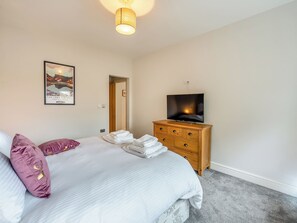 A hotel room with a bed, a wooden dresser, a television, and a framed picture on the wall.