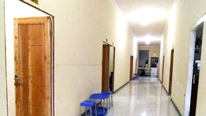A hallway with wooden doors, blue chairs, and a tiled floor. - Hotel O Wisma Air Mancur Homestay Syariah (Tumpang)