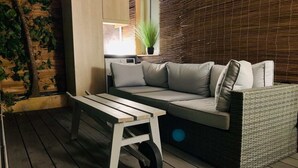 Un espacio al aire libre acogedor con un sofá de mimbre, una mesa de madera y una planta en maceta.