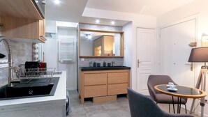 Cocina compacta con electrodomésticos modernos, comedor con mesa y sillas, y un espejo grande sobre el lavamanos.