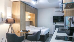 Una habitación de hotel moderna con una cama, un escritorio, dos sillas, una lámpara, un televisor y un minibar.
