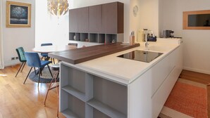 A modern kitchen with a central island, built-in cabinets, pendant lighting, and a dining area with chairs. - Modern apartment with 3 bedrooms, balcony, communal garden and A/C- Benakey (Cannes)