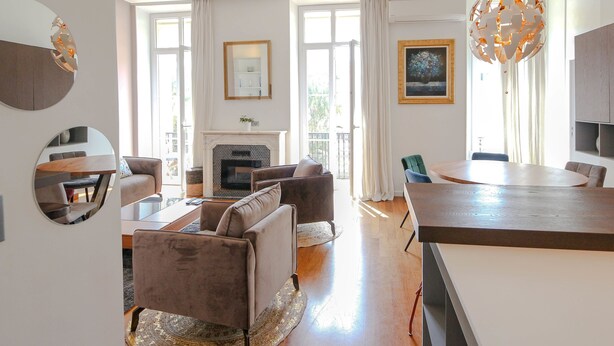 A spacious living room with a fireplace, a dining area, and a kitchen. There are large windows allowing natural light, and the room has a modern design with a chandelier. - Modern apartment with 3 bedrooms, balcony, communal garden and A/C- Benakey (Cannes)
