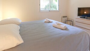 A bedroom with a bed, pillows, a TV, and a window.