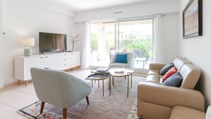 A living room with a sofa, armchair, TV, and a small table. - NEW ! VILLA with Parking, Collective Pools, Garden and AC - BENAKEY (Cannes)