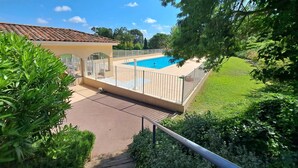 A swimming pool surrounded by a fenced area, with a building in the background and lush greenery around. - NEW ! VILLA with Parking, Collective Pools, Garden and AC - BENAKEY (Cannes)