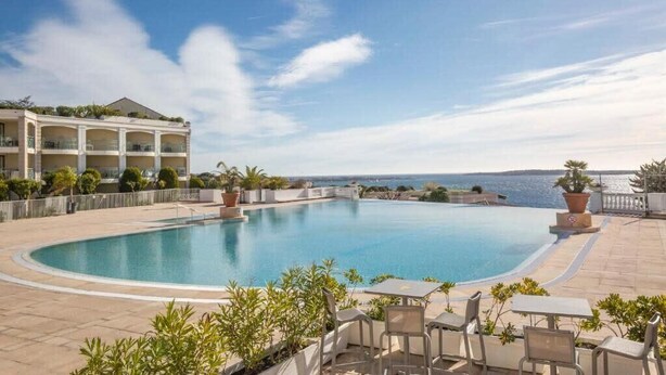Une piscine avec vue sur la mer, entourée de chaises longues et de plantes en pot.