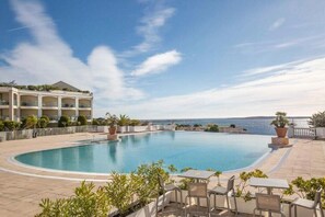 Une piscine avec vue sur la mer, entourée de chaises longues et de plantes en pot.