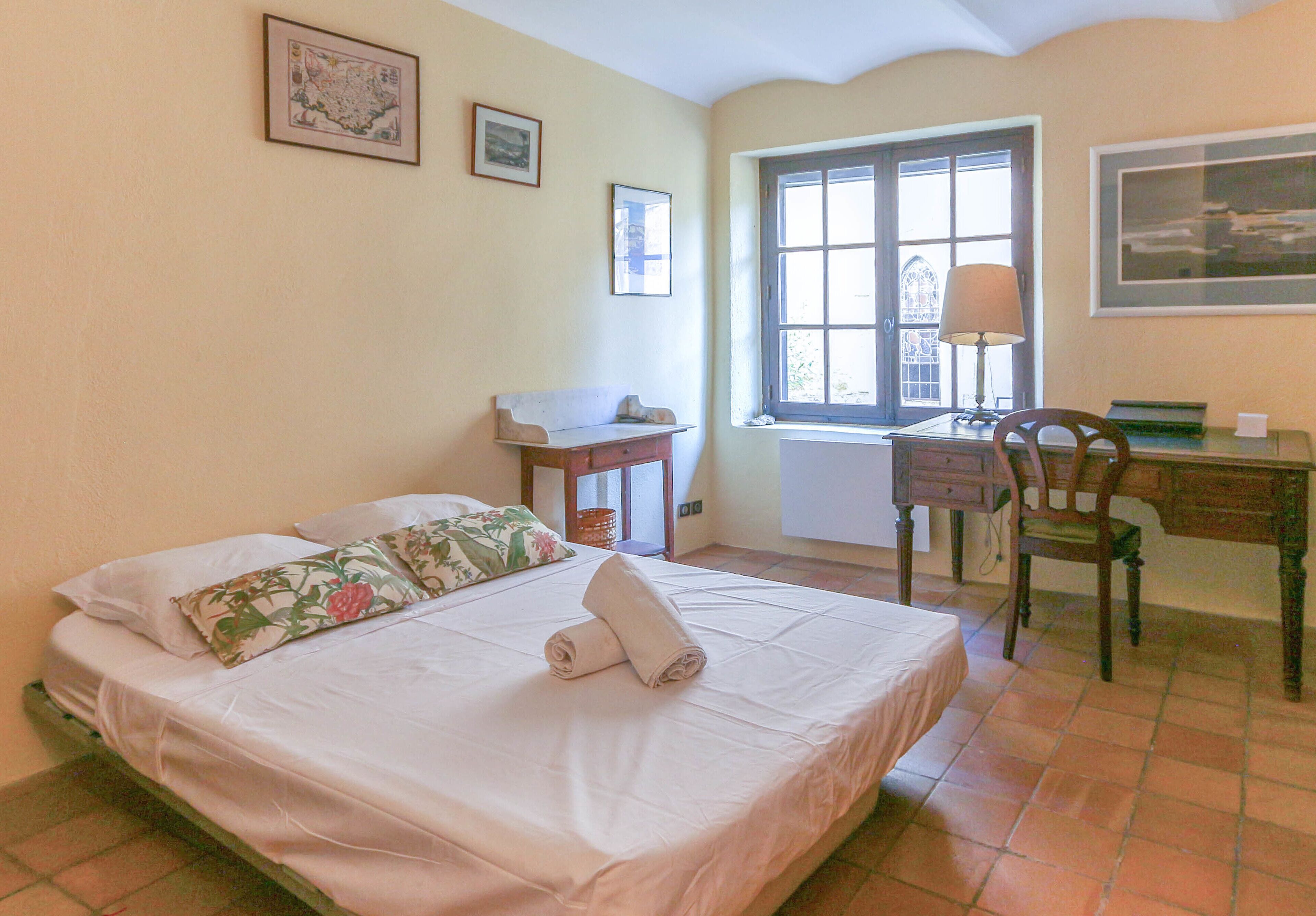 A bedroom with a bed, a desk, a chair, and a window.