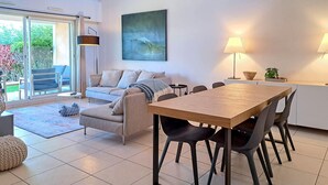 Ein modernes Wohnzimmer mit einer Couch, einem Esstisch mit Stühlen, einer Lampe und einem Bild an der Wand.