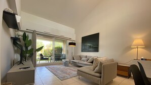 Ein modernes Wohnzimmer mit Sofa, Couchtisch und Lampe. Eine Schiebetür aus Glas führt in einen Außenbereich.