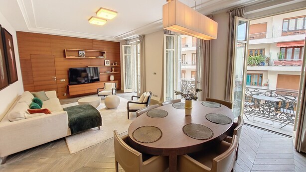 A modern living room with a wooden wall, a flat-screen TV, a sofa, a dining table with chairs, and a balcony with a railing. - N&J - VICTOIRE - Central - Near Beach (Niza)