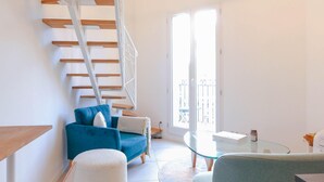 Un salon moderne avec un canapé bleu, un pouf blanc, une table basse en verre et un escalier en bois.