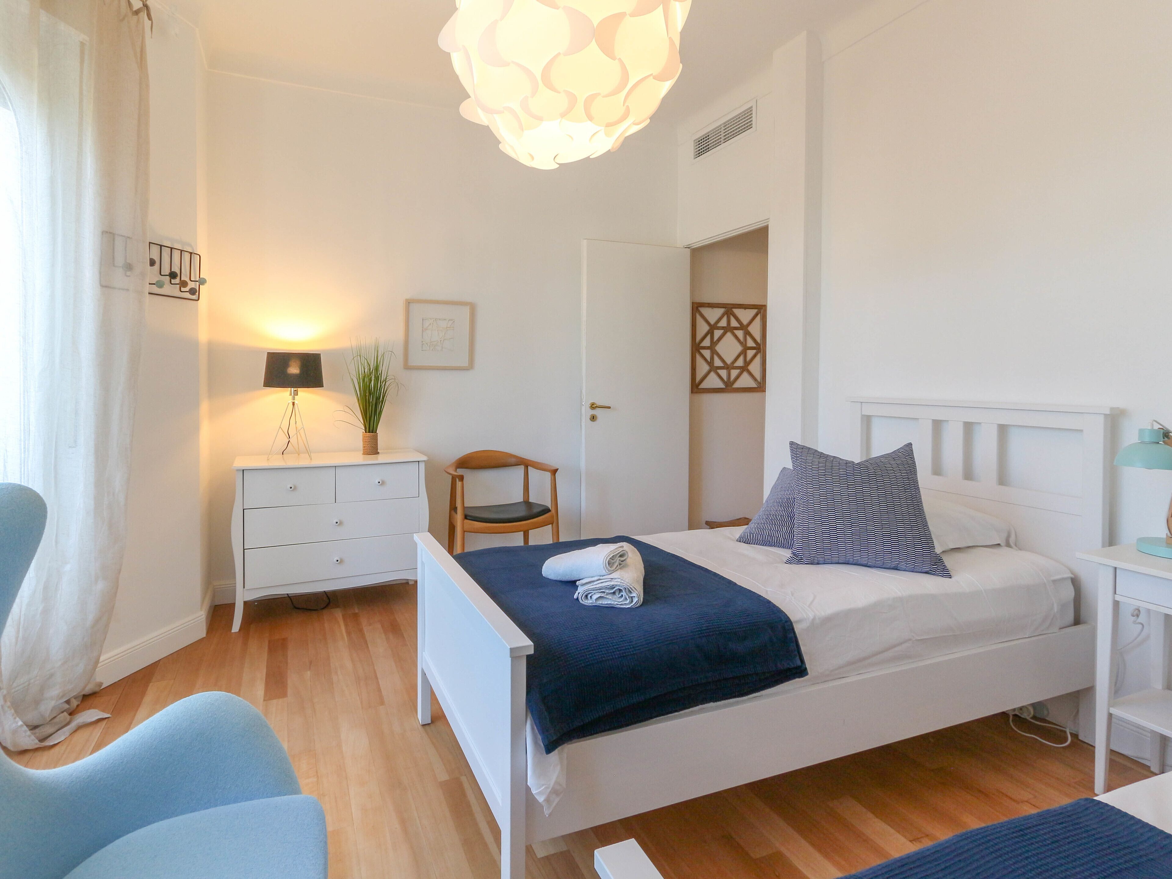 A bedroom with a bed, a chair, a desk, a lamp, a plant, and a wall art piece.