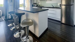Une cuisine moderne dotée d’un îlot central, d’appareils électroménagers en acier inoxydable et offrant une vue sur l’extérieur.