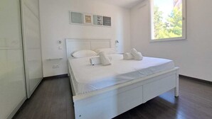 Une chambre moderne avec un grand lit, une armoire et une fenêtre donnant sur un paysage verdoyant.