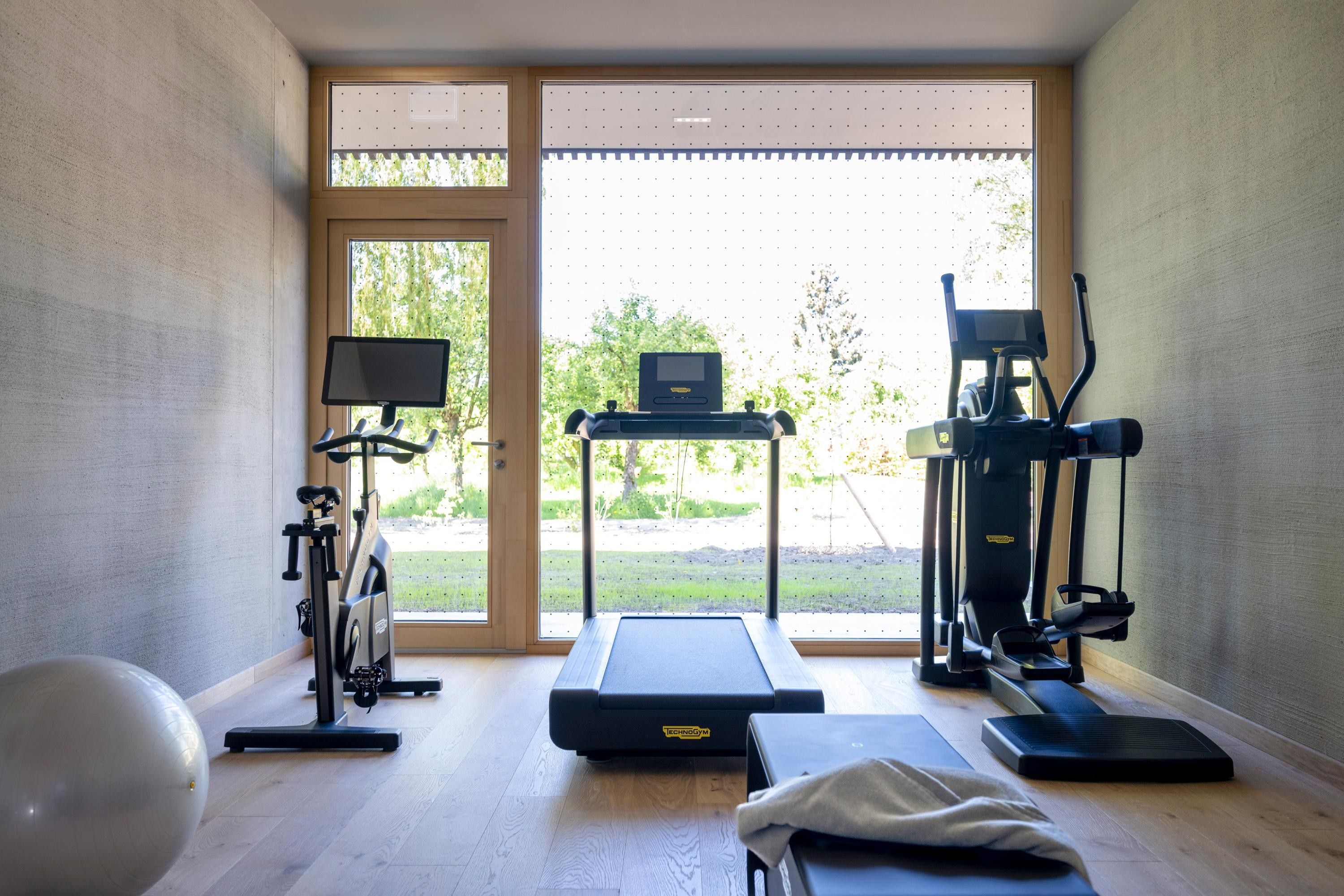 Un gimnasio en casa con cinta de correr, elíptica, bicicleta estática y pelota de ejercicios.