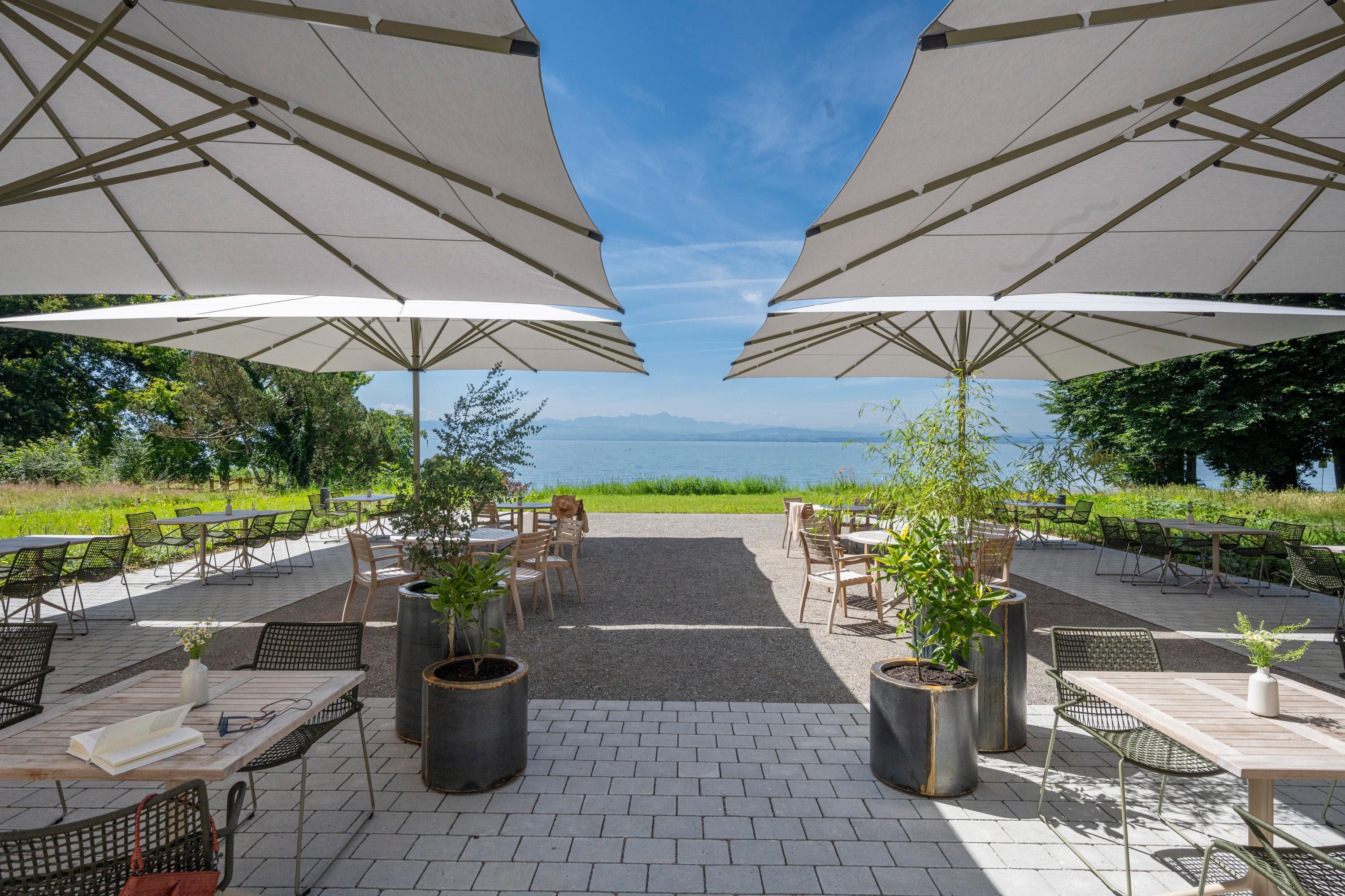 Une terrasse avec des tables et des chaises, de grands parasols et des plantes en pot.