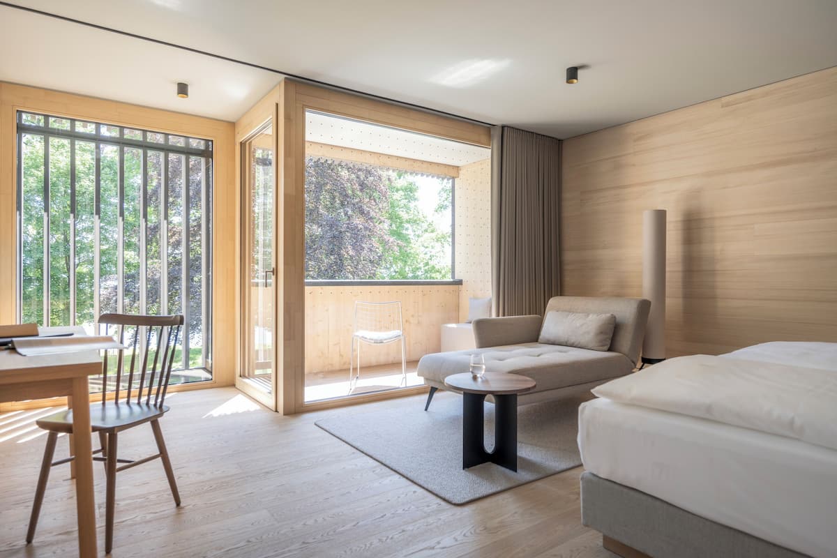 A modern hotel room with a wooden floor, a sofa, a bed, a dining table, and a chair.