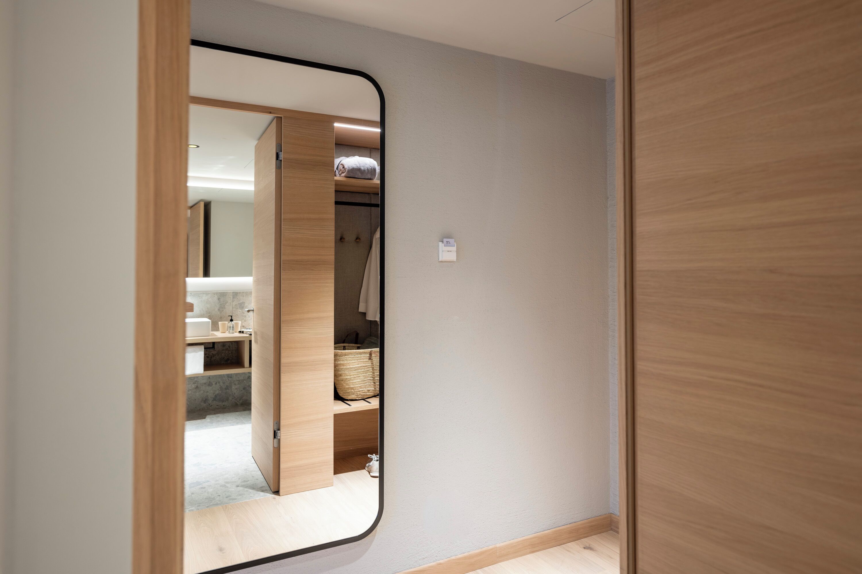 A modern interior with a wooden wardrobe, a mirror reflecting a bathroom with a towel and a basket.