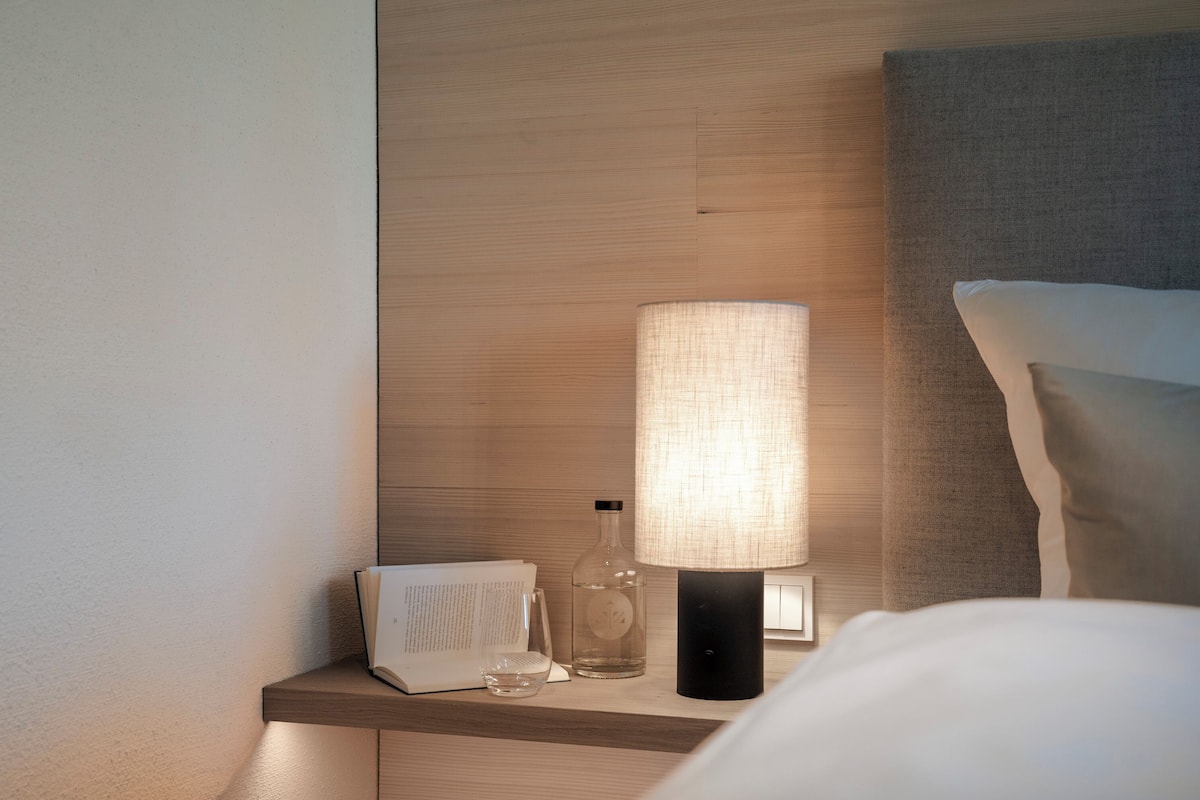 A neatly arranged bedside table with a lamp, a book, and a glass.