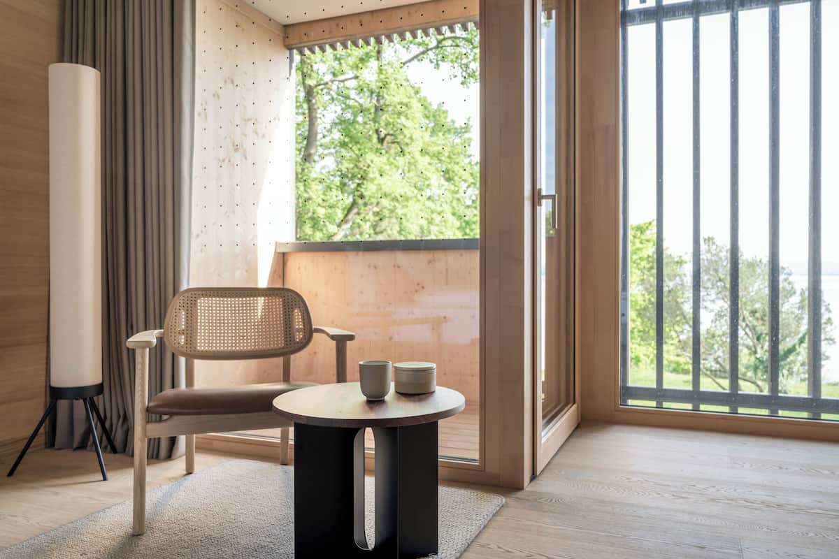 A modern room with a wooden floor, a round table with two cups, a chair, and a large window with a view of trees.